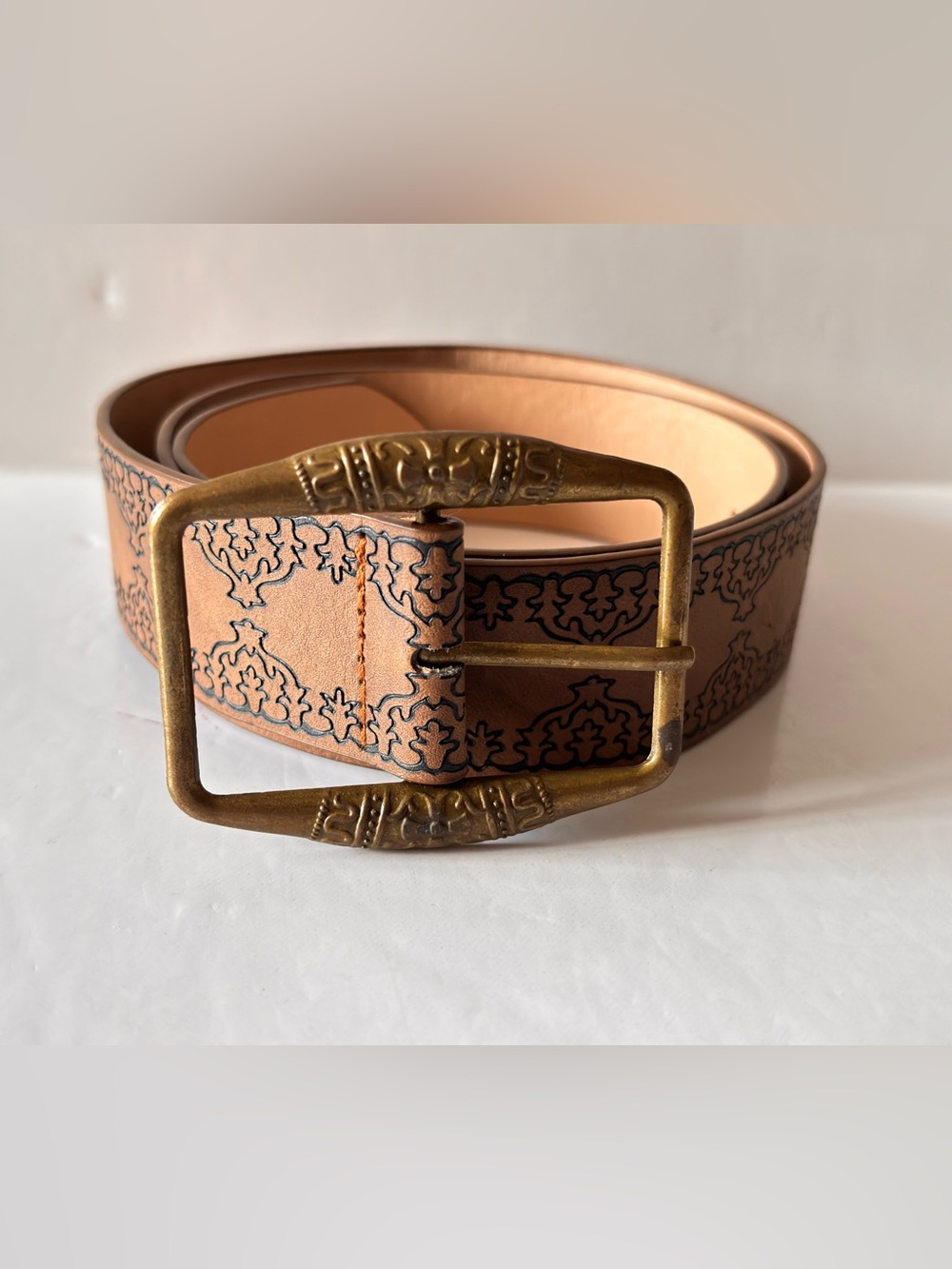 Brown belt adorned with embossed floral patterns and an aged metal buckle